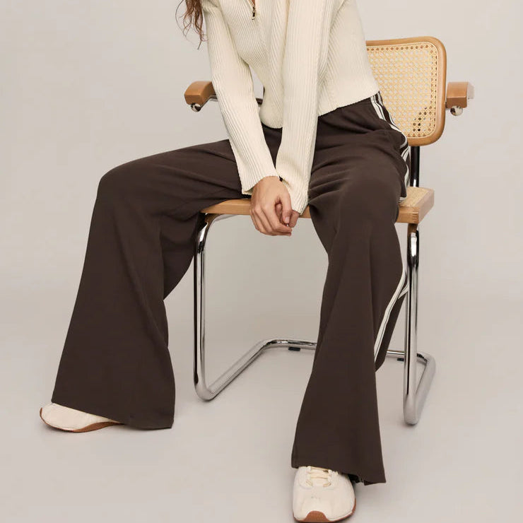 Woman sitting on a chair wearing a white blazer and brown pants against a plain background