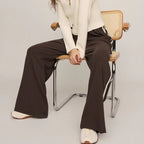 Woman sitting on a chair wearing a white blazer and brown pants against a plain background