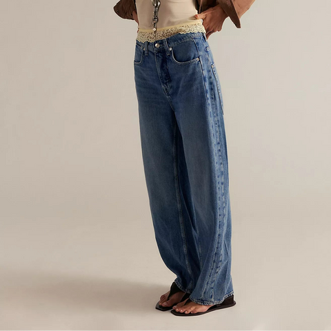 Model wearing Free People Truro Baggy Puddle Jeans in medium blue denim with cream knit belt and brown leather jacket