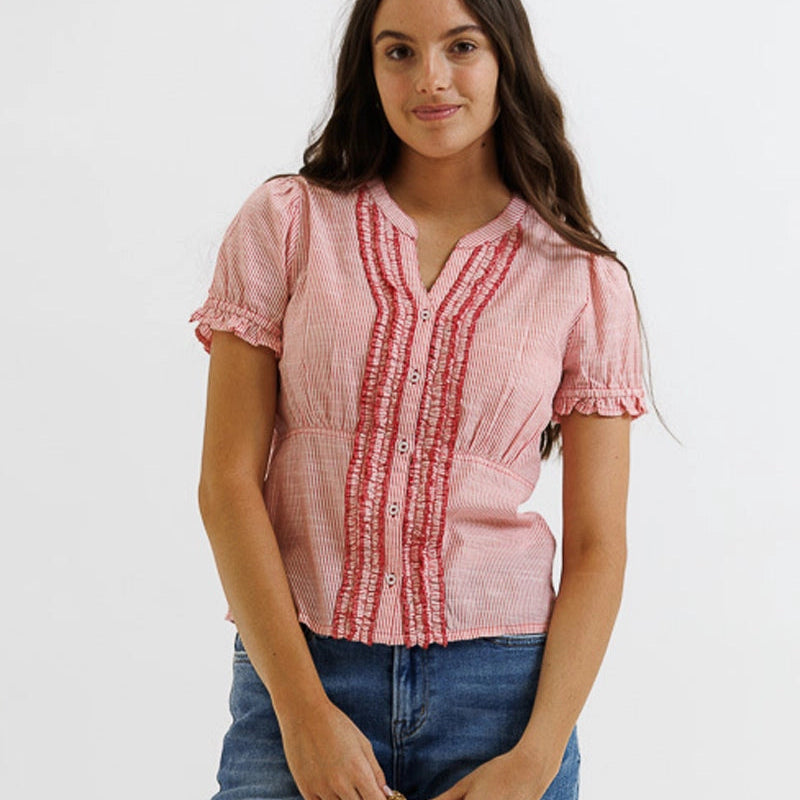 Woman wearing pink and red pinstriped short-sleeve blouse with ruffled neckline and button front, styled with dark denim jea…
