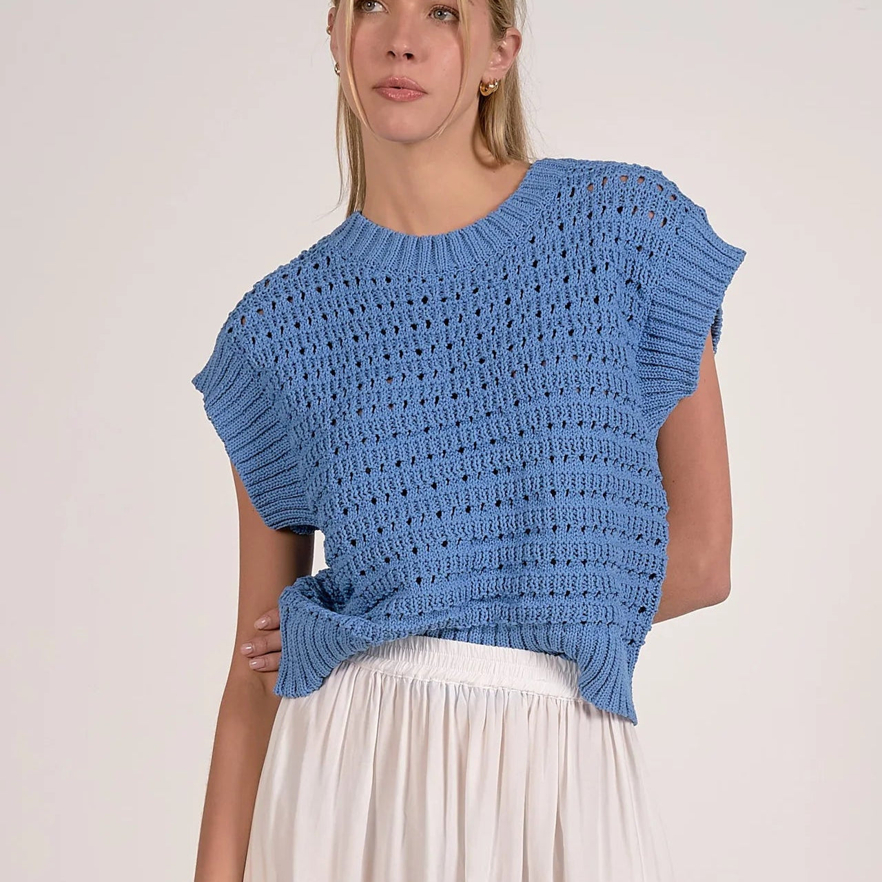 Woman wearing blue open knit sleeveless vest over white skirt, featuring textured knit pattern with small holes throughout