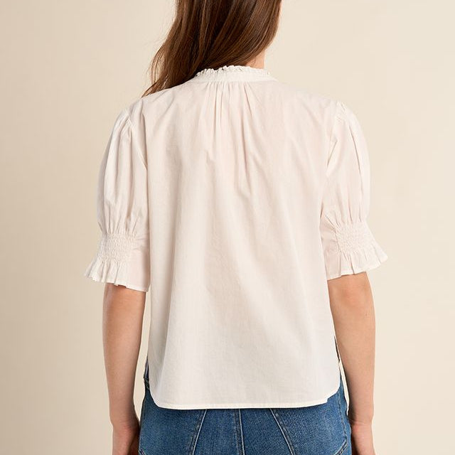 Close-up of a cream-colored blouse with smocked details and buttons.