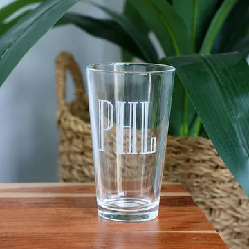 Clear glass with 'PHL' engraving on a wooden surface with plants in the background Main image
